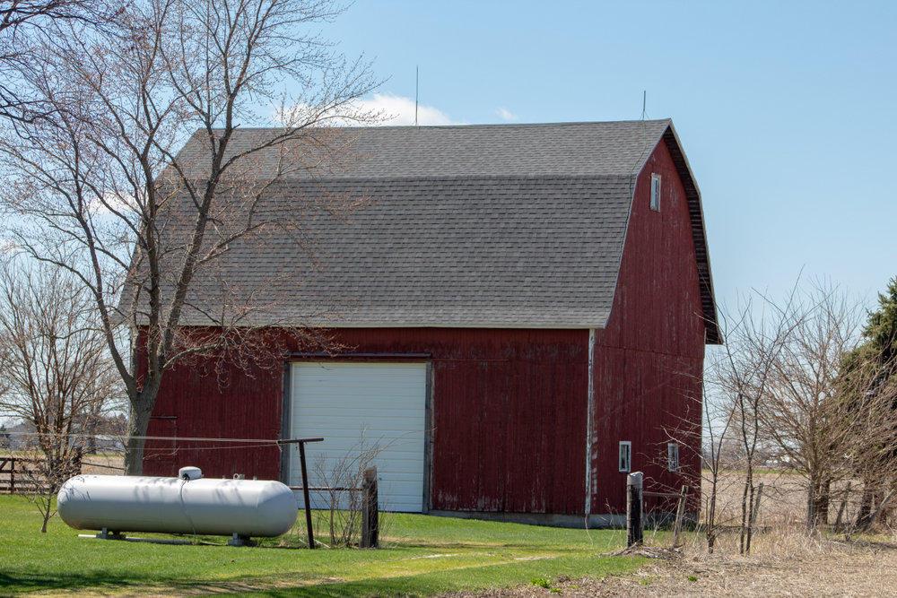 A large propane tank in front of a red barn